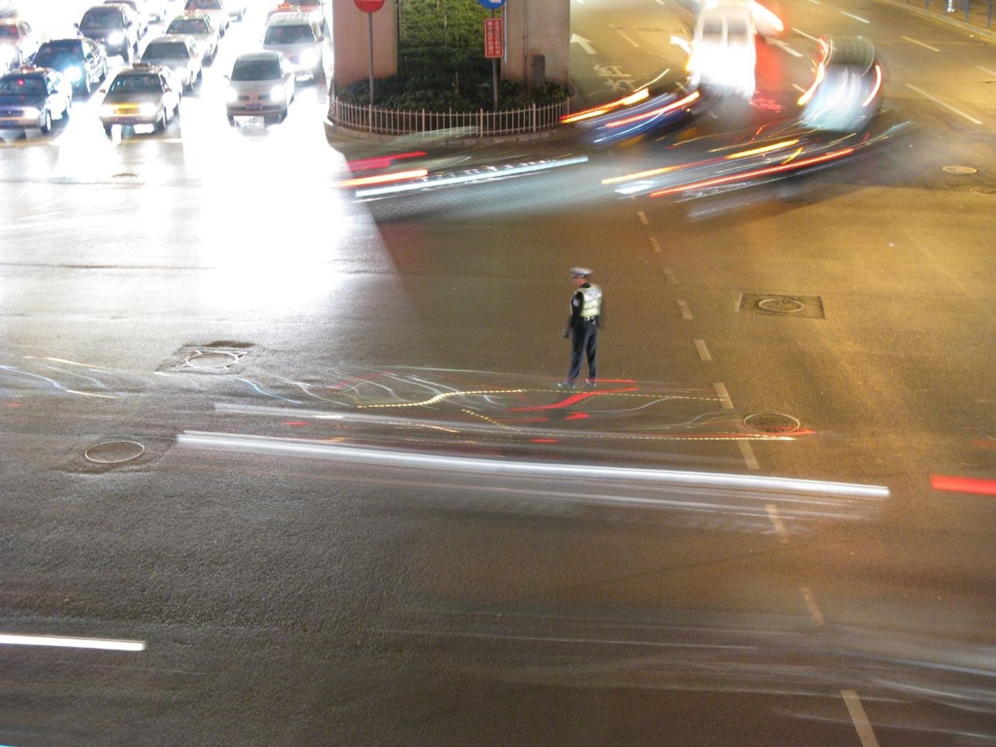 夜间城市路口,长曝光下的车流光轨,路中央有执勤的交警